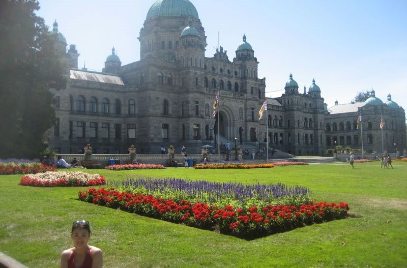 大きな建物の前の庭に立ち、ほほ笑む女性の写真